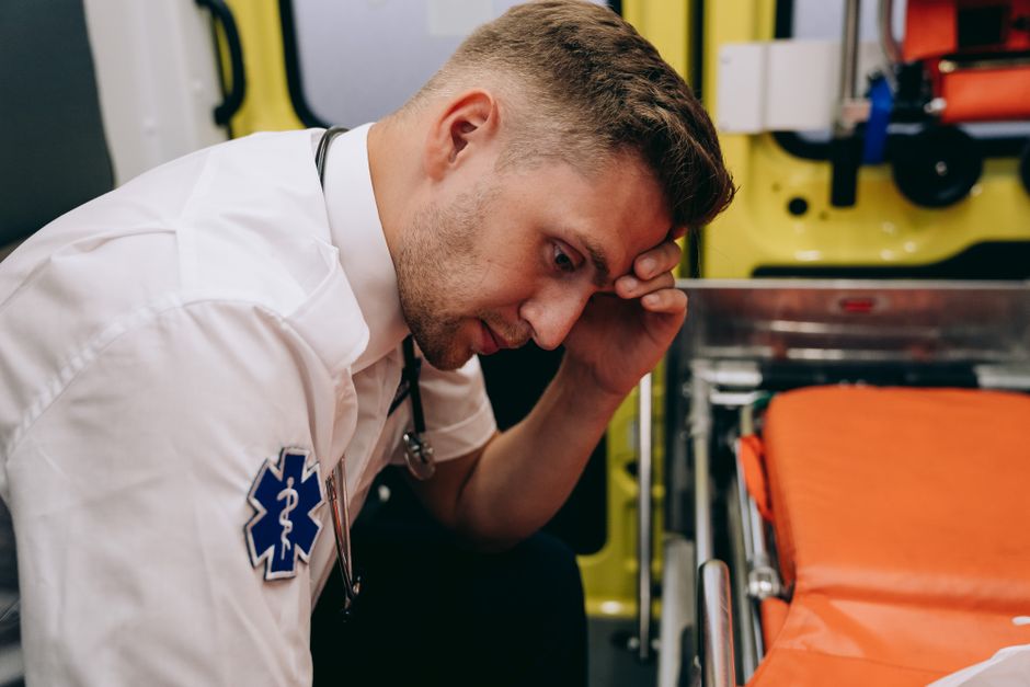 A tired paramedic sitting in an ambulance, hand on head, indicative of stress.